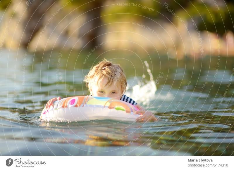 Little boy swimming with colorful floating ring in sea on sunny summer day. Cute child playing in clean water. Family and kids resort holiday during summer vacations.