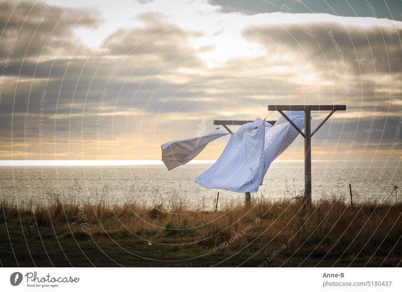 White bed linen waving in the wind on a meadow next to the sea in wonderful backlight and slightly cloudy sky. Laundry leash out dries Wind Weather Sea Wind