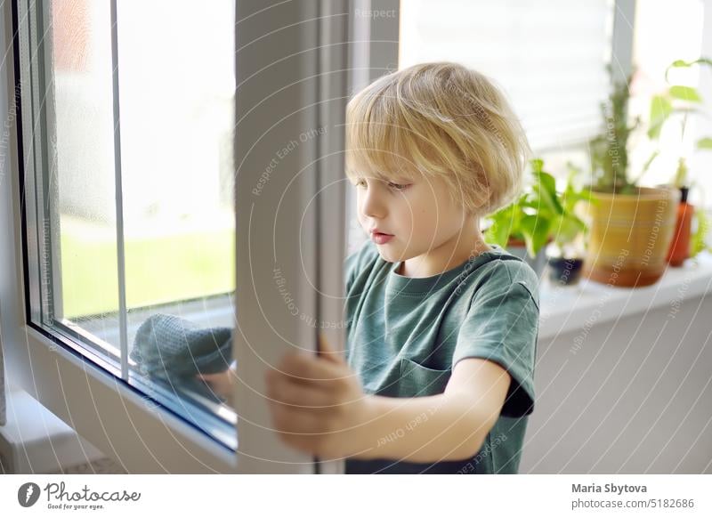 Cute little boy washing a window at home. Child helping parents with household chores, for example, cleaning windows in his house. Children doing housework.