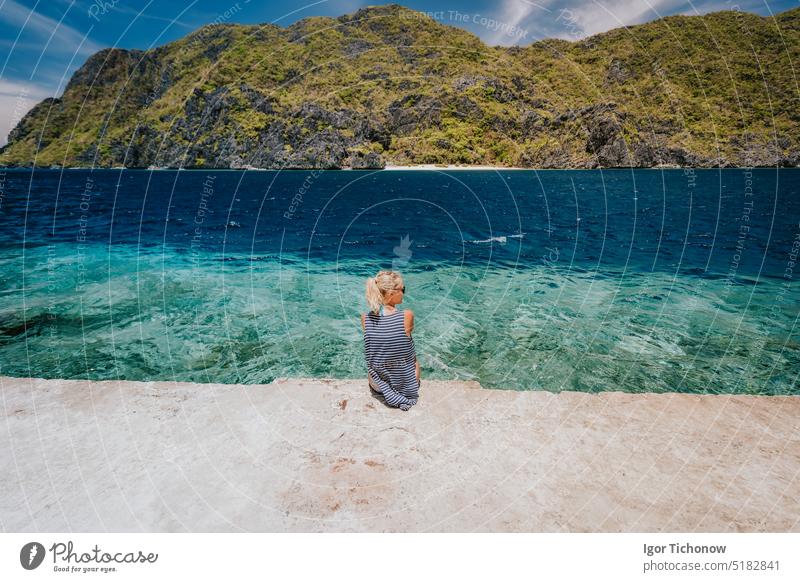 Tourist female rear view sitting pier edge on Matinloc island on hoping tour C. El Nido, Palawan, Philippines nido palawan philippines el turquoise tropical