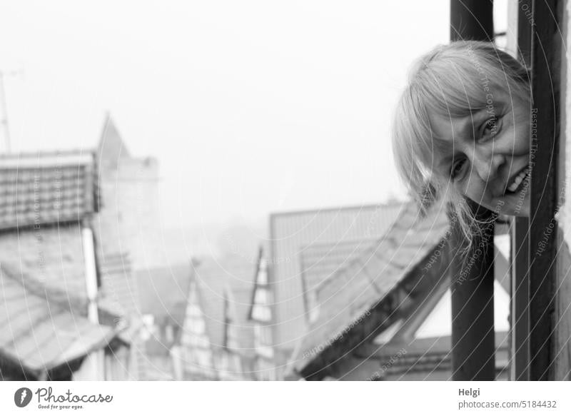 Face of smiling woman looking out of window above roofs of historical city Human being Woman Head hair Smiling outlook Window Town Old town Historic Building