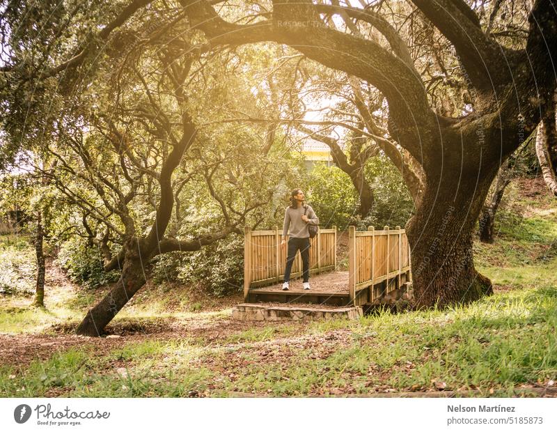 Man walking in a natural park with a backpack on his back with trees and a beautiful sunlight landscape bridge path lifestyle summer wood hanging vacation