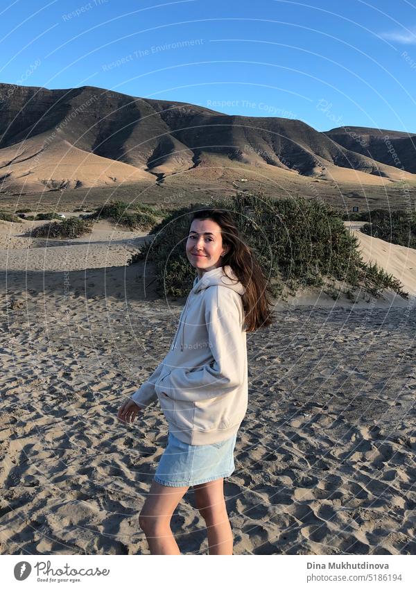 Young woman relaxed on vacation, standing on the beach near mountains, in sunset light, smiling. Real people. Authentic image of real people. beautiful