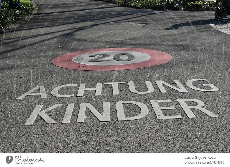 Street with sign for speed limit 20 kilometer per hour and inscription in German language saying attention children. The speed limit and the inscription are marked on the ground.