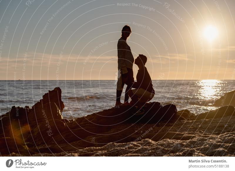 Silhouette of pregnant couple on the rocks watching the sunset. active background beach business clouds construction dusk environment evening freedom girl hand