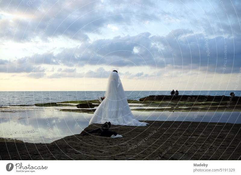 Traditional Turkish bride and groom in summer on the pink rocks in the light of the setting sun behind dramatic clouds on the Black Sea coast in Kefken in Kocaeli province in Turkey