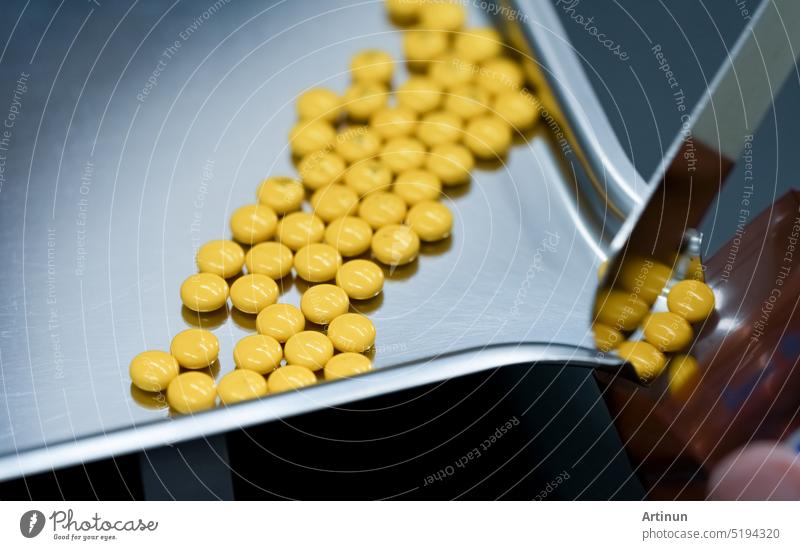 Selective focus on yellow tablets pills on stainless tray with blur hand of pharmacist or pharmacy technician counting pills into a plastic zipper bag. Prescription medicine. Medical health care.