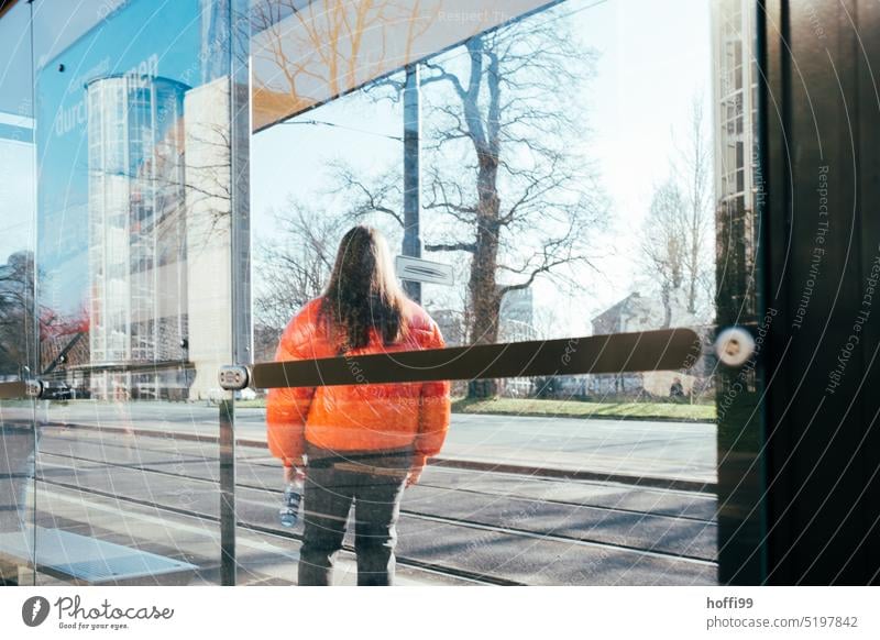 Young person with orange jacket waiting for streetcar at a stop Stop (public transport) Wait Tram Public transit public transportation Means of transport