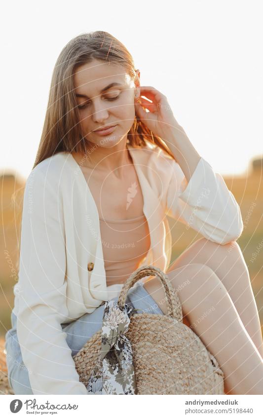 Beautiful portrait of a young woman during the sunset with warm yellow sun rays on her face with bales of straw on the background rural beautiful countryside