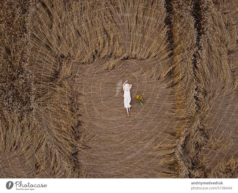 Aerial view of a pretty young woman enjoying the outdoors. girl wearing a white dress lying in wheat field. People, travel, freedom concept. female model nature