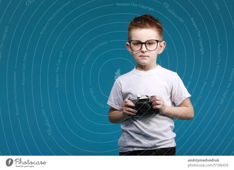 Little boy taking a picture using a retro camera. Child boy with vintage photo camera isolated on blue background. Old technology concept with copy space. Child learning photography