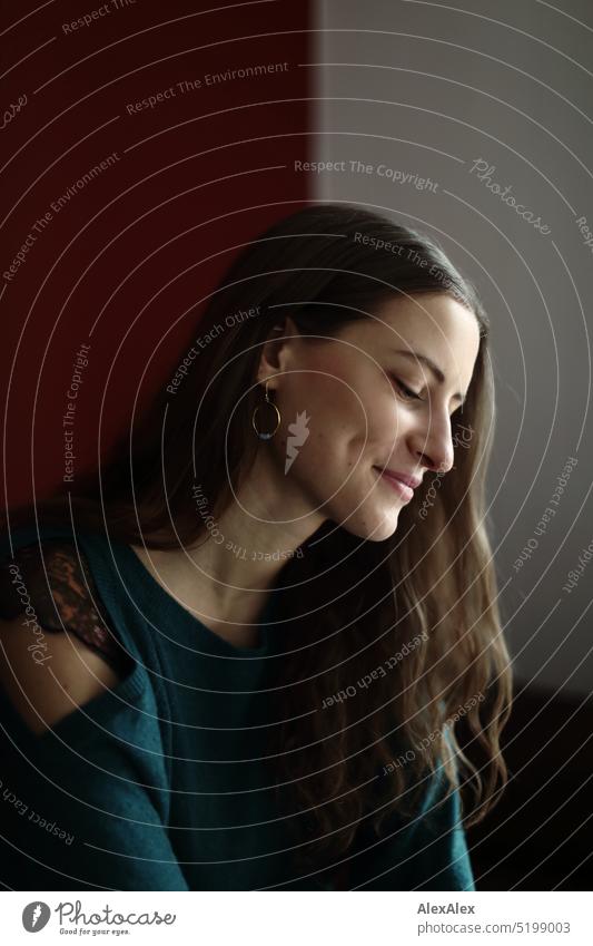 side portrait of young brunette woman with dimples on cheeks wearing off shoulder sweater sitting in front of red wall Face Face of a woman Woman Young woman