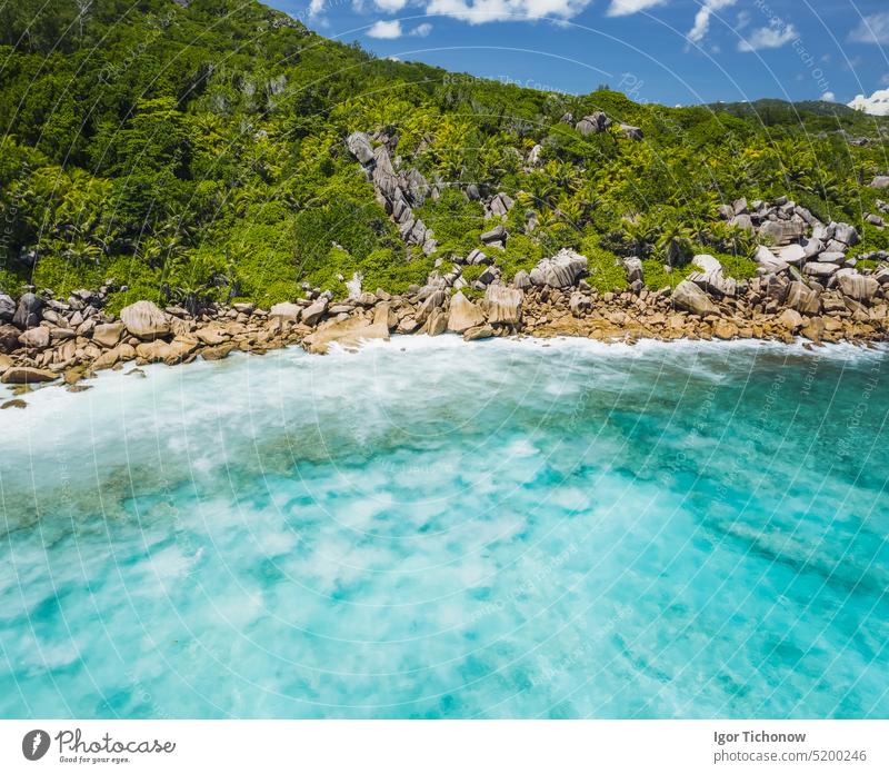 Aerial drone view of tropical paradise like beach with pure crystal clear turquoise water, bizarre granite rocks and coconut palm trees. Travel concept aerial