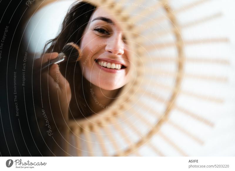 Young happy woman appying make up in front of a round mirror young brush cosmetic applying make-up smile smiling toothy powder blush face attractive girl