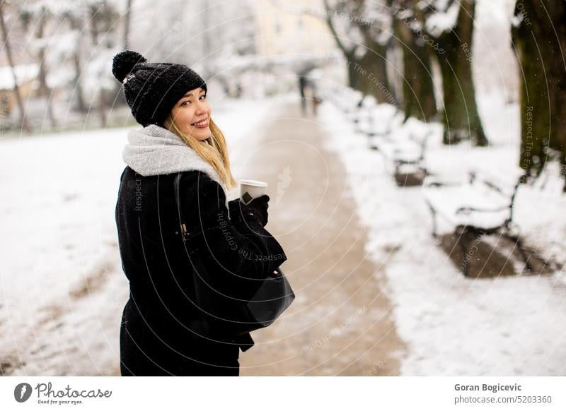 Young woman with Warm Clothes in Cold Winter Snow drinking coffee to go adult black clothing coat cold temperature glove hat one person portrait snow spring