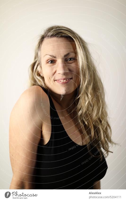 side portrait of blonde long haired woman in black tank top Woman Blonde Long-haired Smiling Looking into the camera Slim daintily pretty naturally Emanation