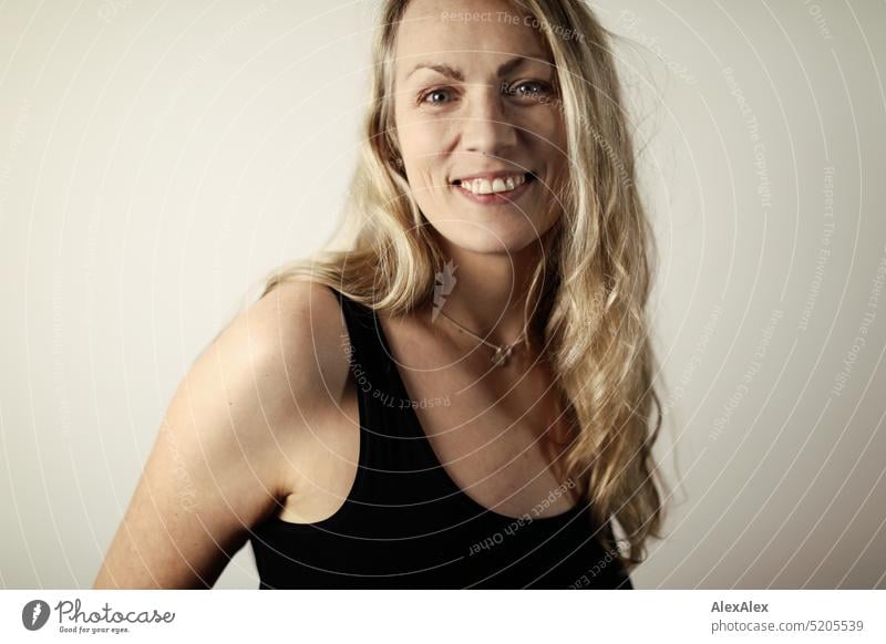 side portrait of blonde long haired woman in black tank top Woman Blonde Long-haired Smiling Looking into the camera Slim daintily pretty naturally Emanation