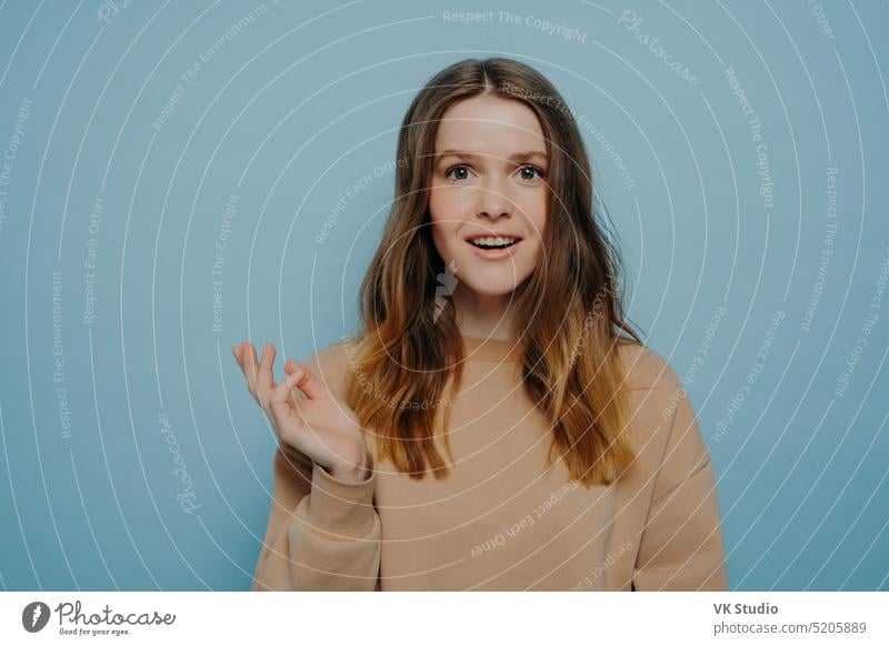 Pretty young girl showing amusement and surprise posing against blue wall woman positive excited happy amused teen teenage amazement smiling demonstrating