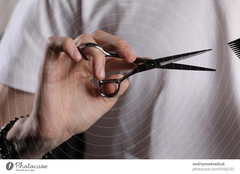 Barber in white t shirt holding scissors, background is blurred. Concept of men style. Professional tools of hairdresser. Professional occupation, art, self-care concept. Magazine. copy space