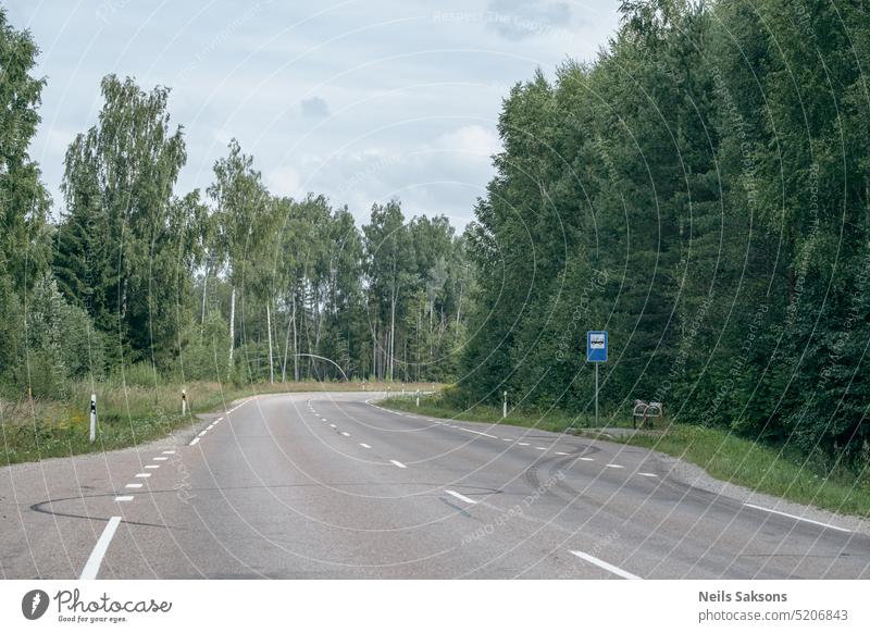 empty asphalt road in green summer forest with trees and grass. perspective, bus stop in Latvia countryside background beautiful blue blue sky curve drive