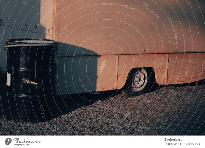 Black barrel stands next to sales cart, one wheel, red morning light and shadow ton Carriage Wheel Shadow Light Morning Red reddishly Mood lighting gravel urban