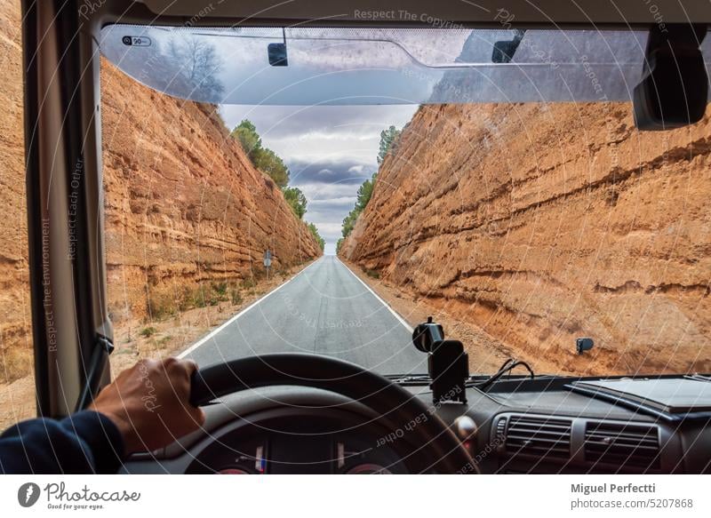 View from the driving position of a truck driving on a narrow road between two cuts dug into the ground, with the truck's dashboard and steering wheel in the foreground.