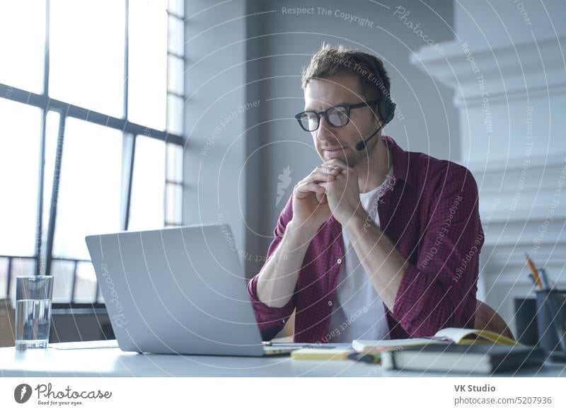 Pensive German businessman in headphones sits at desk while remotely working from home pensive german headset look laptop display talk online video call