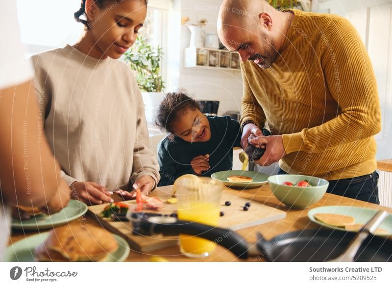 Boy with Down syndrome having pancakes for breakfast with family boy down syndrome multiracial serve eat pour syrup parent four black kitchen food make fun