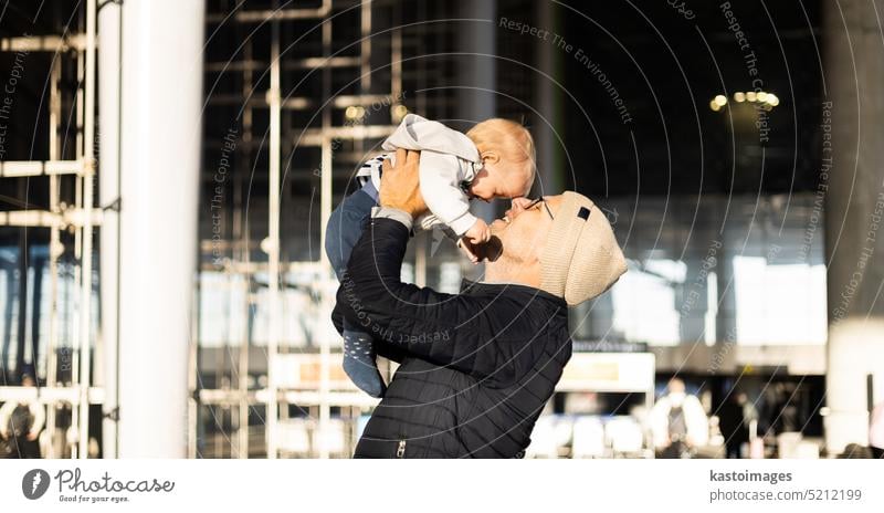 Father happily holding and lifting his infant baby boy child in the air after being rejunited in front of airport terminal station. Baby travel concept. dad