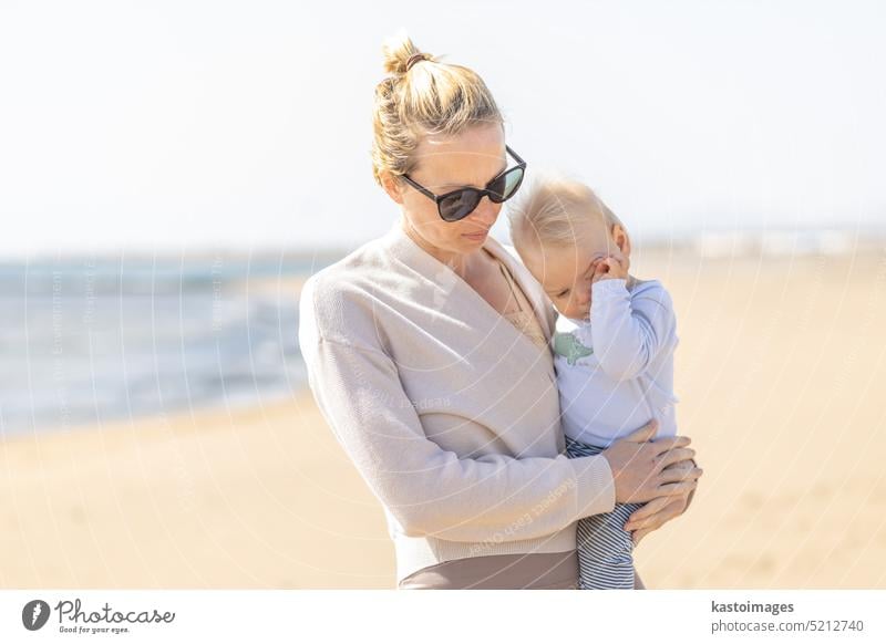 Mother holding and carrying his infant baby boy son on sandy beach enjoying summer vacationson on Lanzarote island, Spain. Family travel and vacations concept.