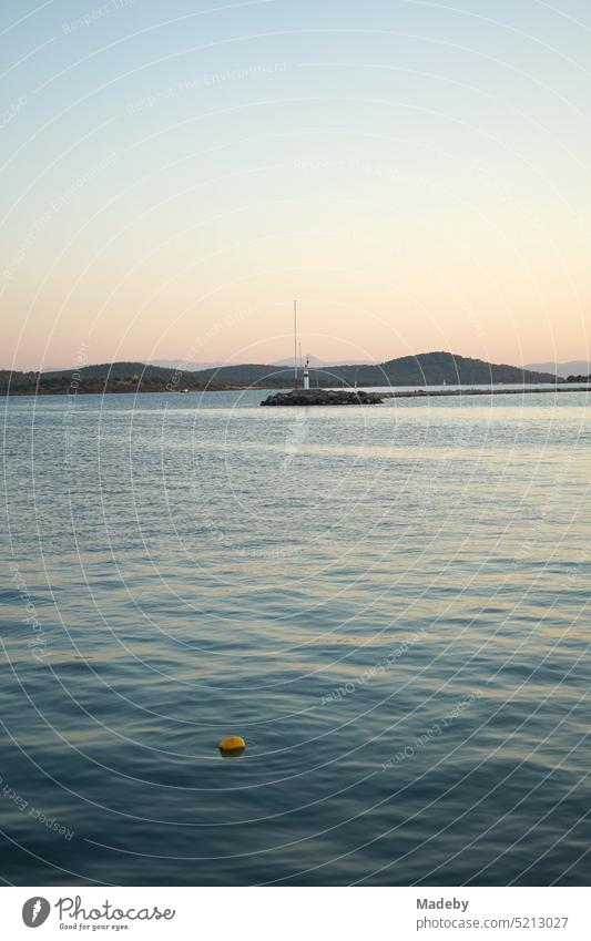 Romantic evening atmosphere at the sea with the light of the evening sun with lighthouse and pier at the harbor in the bay of Ayvalik at the Aegean Sea in the province of Balikesir in Turkey