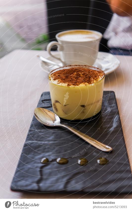 Tiramisu sweet dessert served in Italy with a spoon on a table with a defocused background of a cup of hot cappuccino coffee. Italy served tiramisu