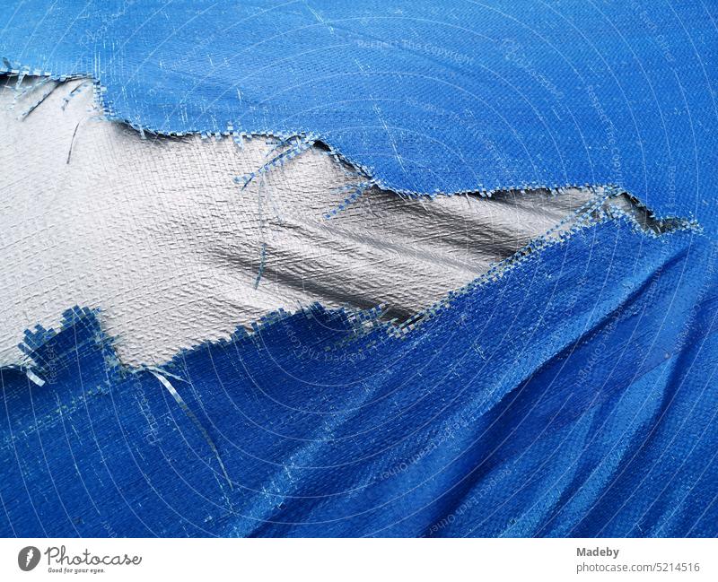 Old torn tarpaulin made of plastic in blue and white on a boat trailer in Oerlinghausen near Bielefeld at the Hermannsweg in the Teutoburg Forest in East Westphalia-Lippe