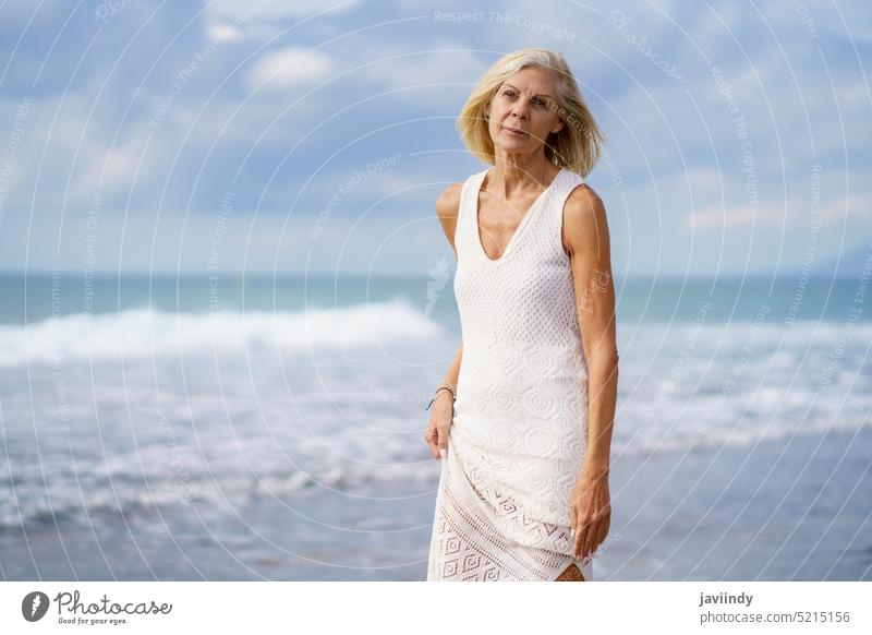 Mature woman walking on the beach. Elderly female standing at a seaside location mature senior old caucasian person elderly retirement lifestyle happy holiday