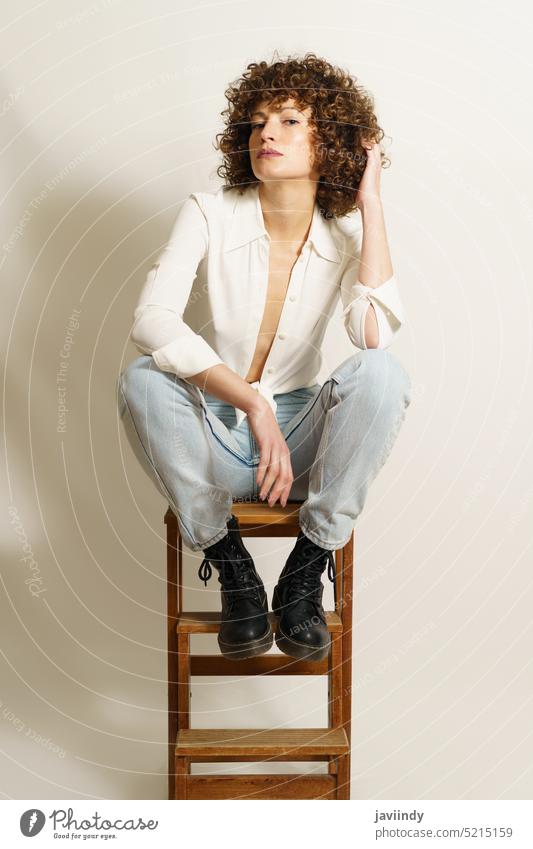 Self confident adult female chilling on ladder woman model rest wooden stool curly hair self confident flirt fashion style casual outfit cloth wear shirt jeans