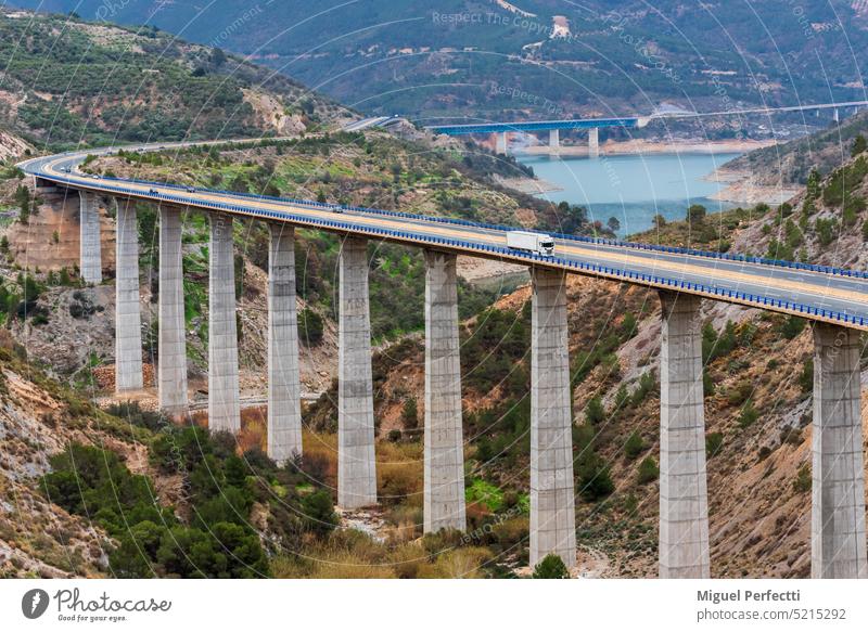 Refrigerated truck driving on a highway with bridges over a swamp, road landscape in the mountains and next to a dam. refrigerator motorway viaduct transport