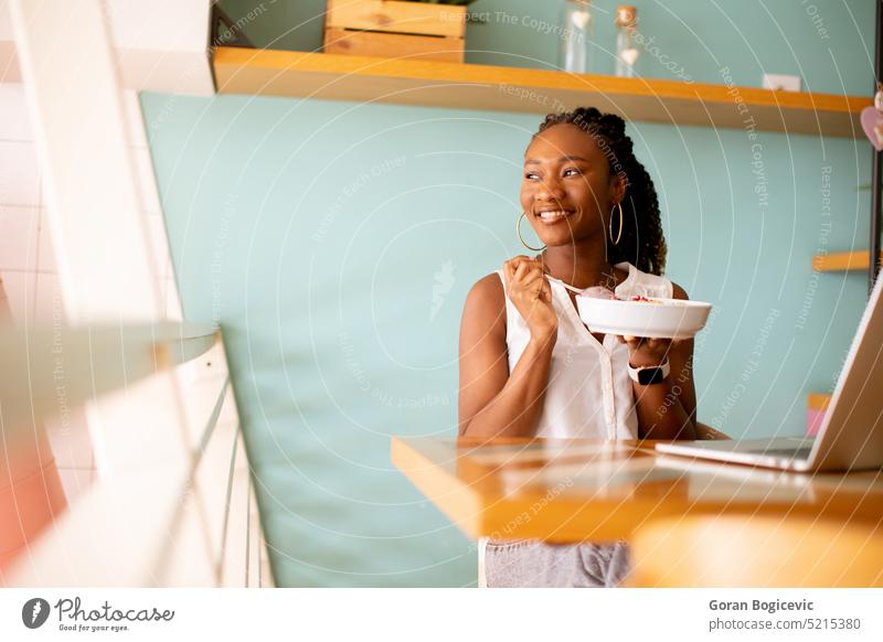 Young black woman having a healthy breakfast while working on laptop in the cafe internet computer modern freelancer happy nutrition young e-learning