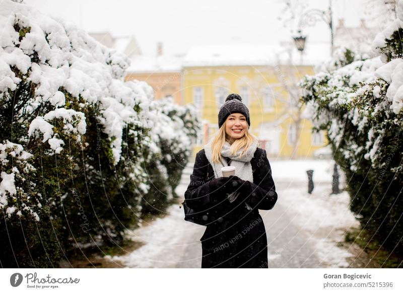 Young woman in warm clothes enjoying in snow with takeaway coffee cup adult air alone beautiful beauty brunette cap charming coat cold cute day emotions female