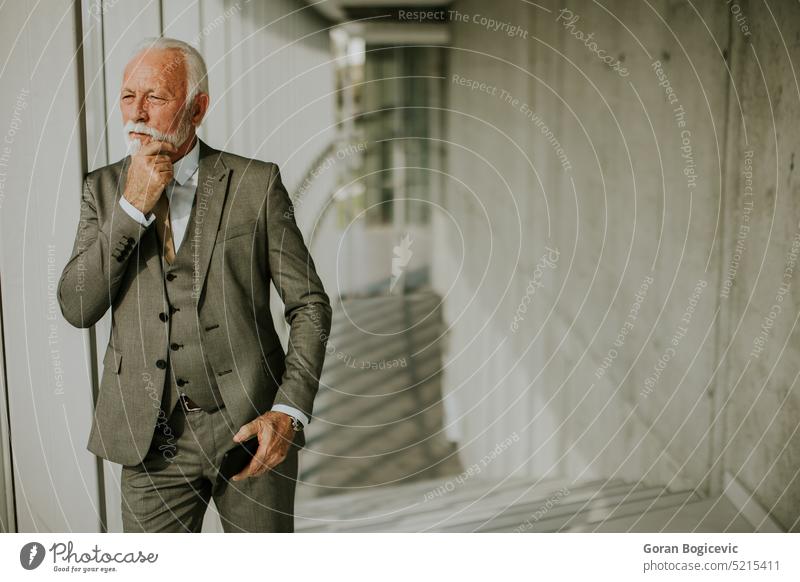 A senior business man stands in an office hallway, focused on his mobile phone ambition business communication business culture business development