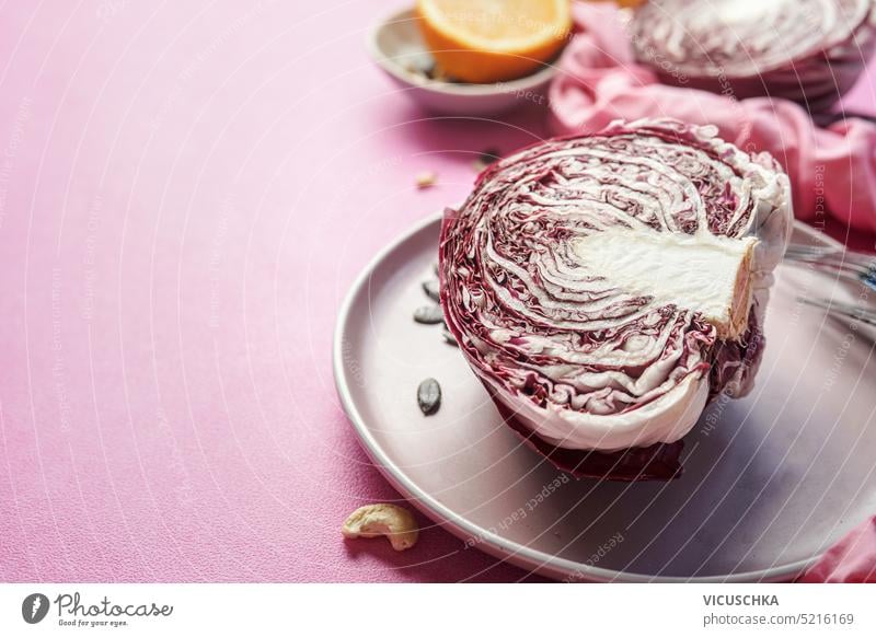 Halved radicchio on plate at pink table background, border halved salad cooking ingredient raw healthy vegetable vegetarian vegan lettuce food