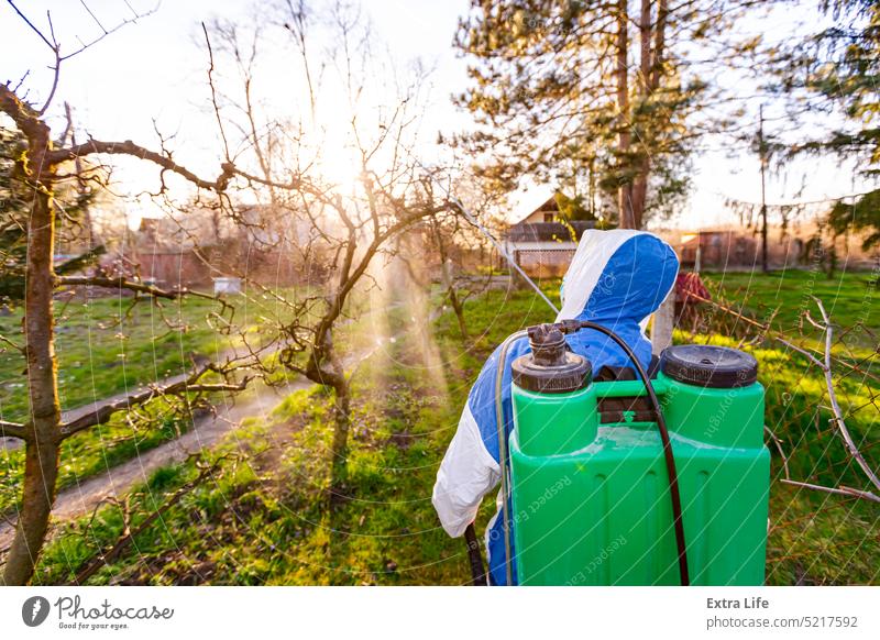 Back view on gardener in protective overall sprinkles fruit trees with long sprayer in orchard Aerosol Agricultural Agriculture Backlight Biochemical Biohazard