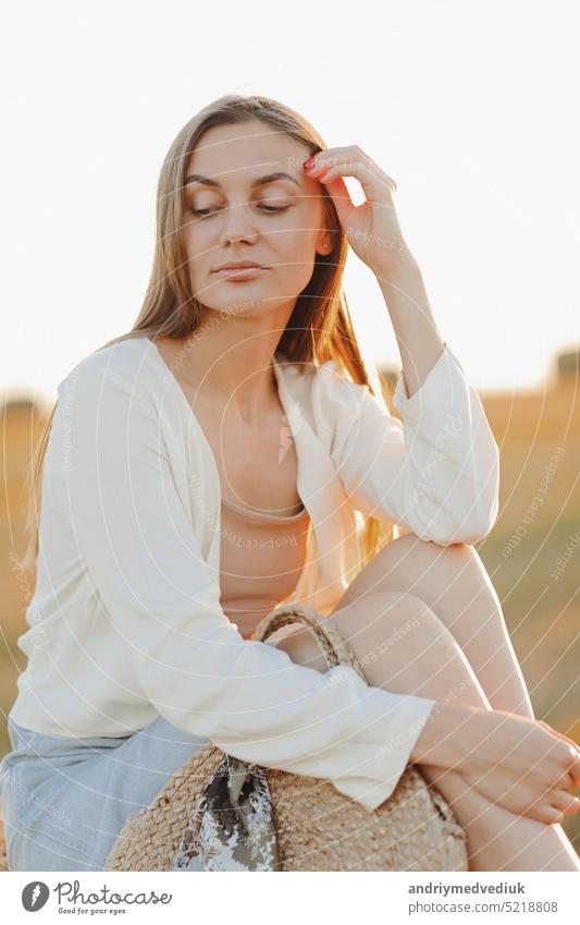 Beautiful portrait of a young woman during the sunset with warm yellow sun rays on her face with bales of straw on the background rural beautiful countryside