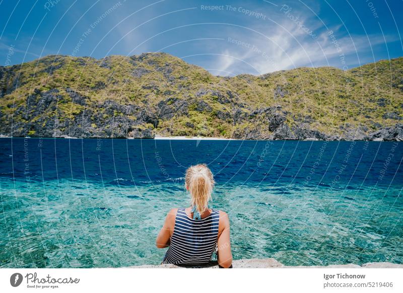 Tourist female rear view sitting on Matinloc dock pier enjoying tapiutan strait on island hoping tour C. El Nido, Palawan, Philippines nido palawan philippines