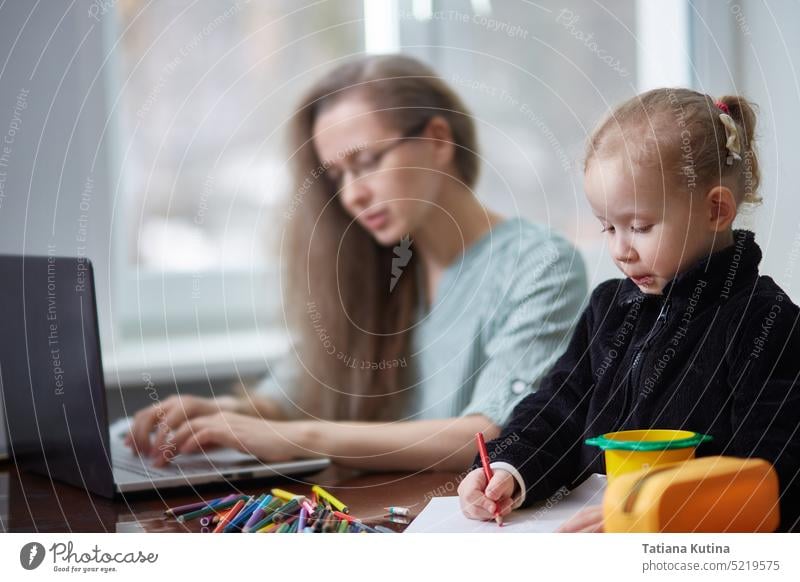 A girl draws with pencils while working as a freelancer's mother. The concept of working at home and taking care of the family. child maternity daughter