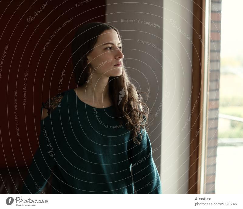 Portrait of young beautiful brunette woman in front of red wall and balcony window from which she looks out Wall (building) Red Sweater Turquoise cryptic