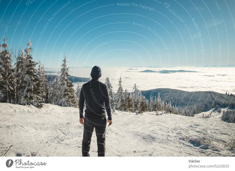 Enthusiastic young traveller enjoys the view from the highest mountain of the Beskydy Mountains in Central Europe of the snowy landscape disappearing in the morning inversion at sunrise