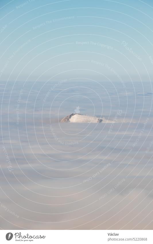 View of the top of Mount Skalka in the Beskydy Mountains under the cover of thick white fog in the morning hours. Snowy hills with clouds. Being above the clouds