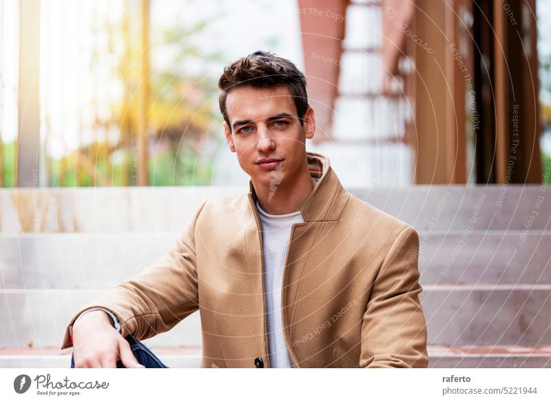 Portrait of stylish handsome young man with coat sitting outdoors Adult Camera Caucasian Confidence Elegance Inspiration Jacket Leaning Lifestyle Male Modern