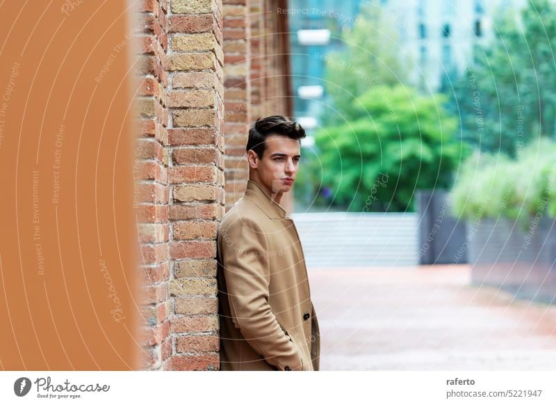 Young man wearing winter clothes in the street. Young guy with modern hairstyle with brown coat. Adult Caucasian Jacket Leaning Lifestyle Male Modern Outdoors