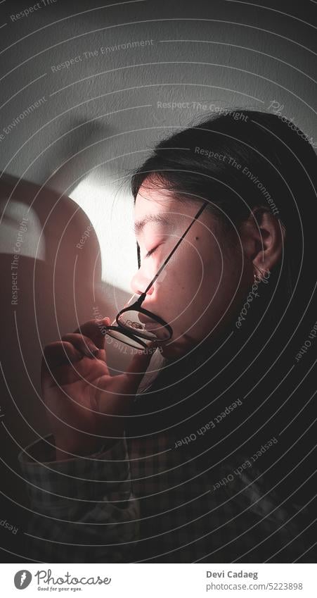 A girl in a dark room removing her glasses and eyes closed girl in glasses Girl portrait young face person people Portrait photograph lifestyle